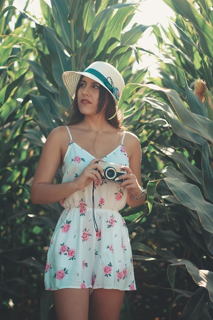 Retrato de estilo de vida al aire libre de una joven hermosa morena con cámara de fotos vintage con un vestido florido y sombrero para el sol