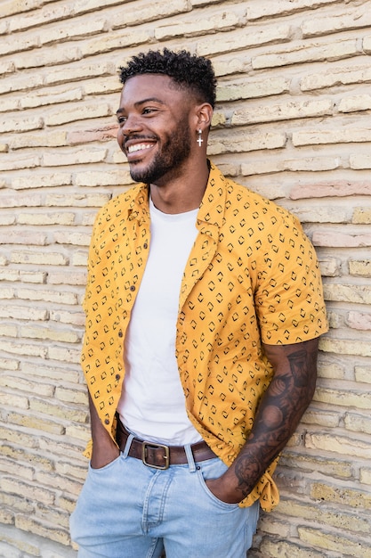 Retrato de estilo de vida de un atractivo y joven con barba sonriendo y apoyado contra una pared de ladrillos