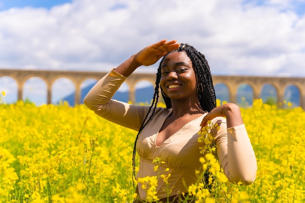 Retrato de estilo de vida de una chica étnica negra con trenzas en un campo de flores amarillas