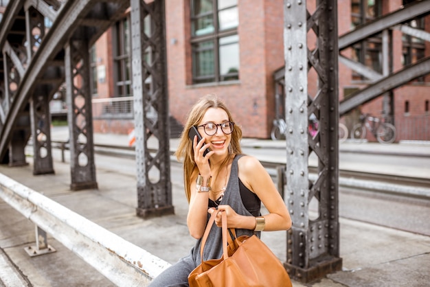 Retrato de estilo de vida de una elegante mujer de negocios sentada con teléfono al aire libre en el puente de hierro