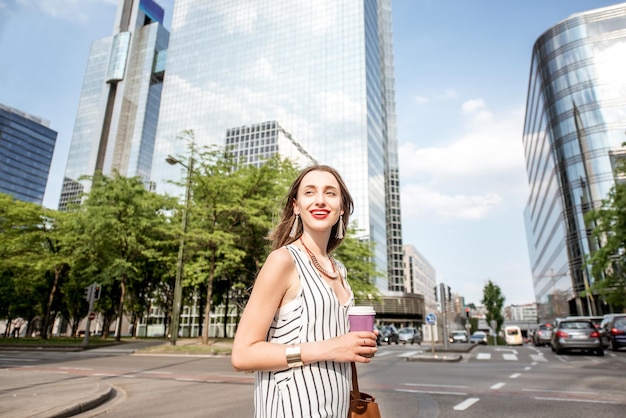 Retrato de estilo de vida de una empresaria con café cruzando la calle en el moderno distrito de oficinas en Bruselas, Bélgica