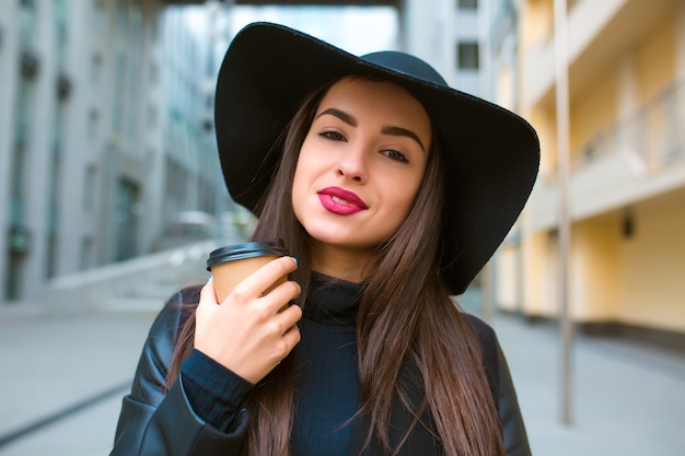 Retrato de estilo de vida de la hermosa modelo morena con taza de café con sombrero de ala ancha. Café para llevar concepto