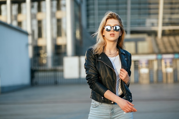 Retrato de estilo de vida de una joven impresionante con gafas de sol de espejo y chaqueta de cuero. Espacio para texto