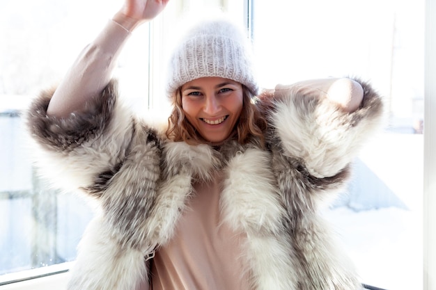 Retrato de estilo de vida de moda de una joven mujer de moda vestida con un abrigo de piel blanco de hata de punto azul posando y sonriendo en el retrato de invierno de una mujer alegre