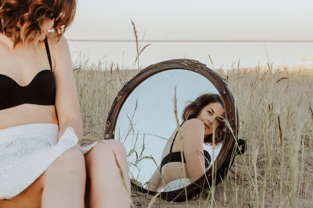 Retrato de estilo de vida de moda de mujer romántica joven d sentado en la playa en el reflejo del espejo