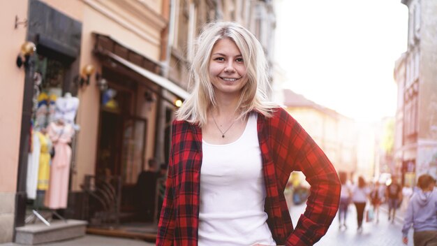 Retrato de estilo de vida de la moda rubia feliz con el pelo despeinado chica con una camisa roja rock, camiseta blanca divirtiéndose al aire libre en la ciudad