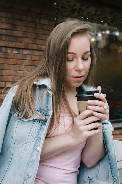 Retrato de estilo de vida de una mujer blanca adulta joven sosteniendo una taza de café para llevar al aire libre, enfoque selectivo