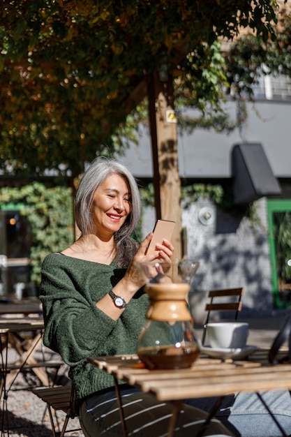 Retrato de estilo de vida de mujer elegante cabello pálido maduro al aire libre cerca de cafe