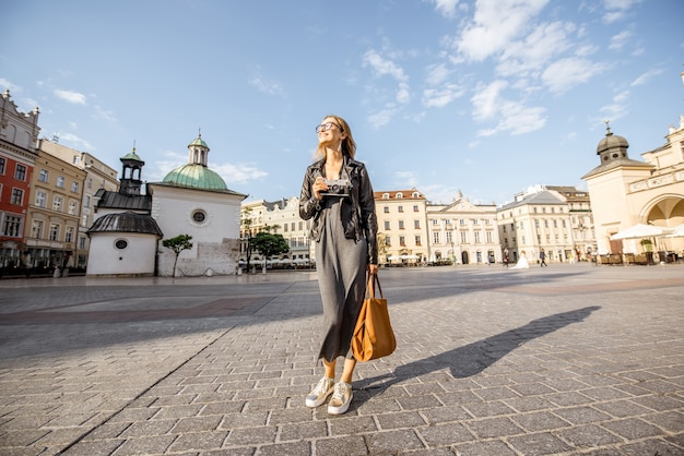 Retrato de estilo de vida de una mujer elegante caminando en la plaza del mercado durante la luz de la mañana en Cracovia, Polonia