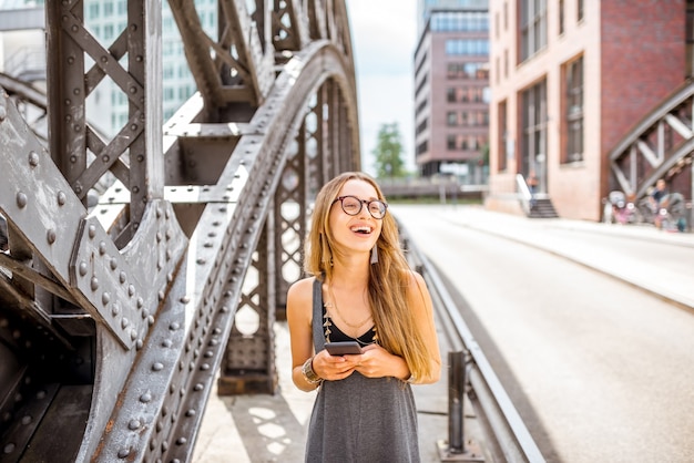 Retrato de estilo de vida de una mujer joven y elegante caminando con smartphone al aire libre en el viejo puente de hierro