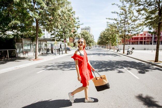 Retrato de estilo de vida de una mujer en vestido rojo cruzando la calle en el distrito moderno de la ciudad de Barcelona