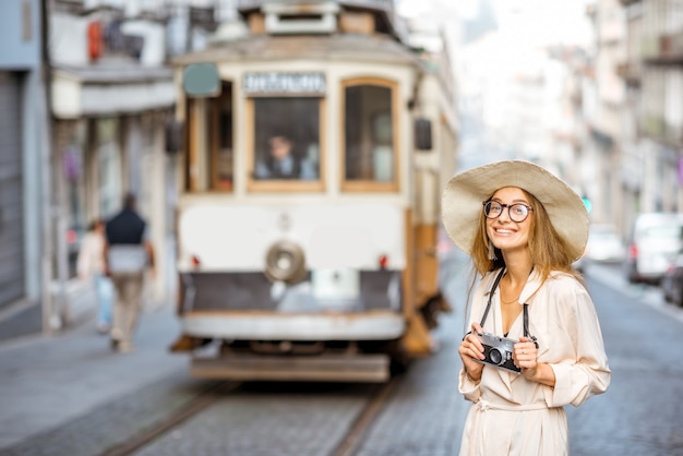 Retrato de estilo de vida de una mujer viajera de pie en la calle con el famoso y antiguo tranvía turístico en el fondo en la ciudad de Oporto, Portugal