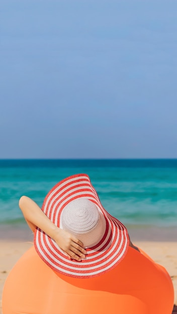 Retrato de estilo de vida de verano de una chica guapa sentada en el sofá inflable naranja en la playa de