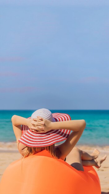 Retrato de estilo de vida de verano de una chica guapa sentada en el sofá inflable naranja en la playa de