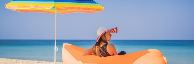 Retrato de estilo de vida de verano de una chica guapa sentada en el sofá inflable naranja en la playa de