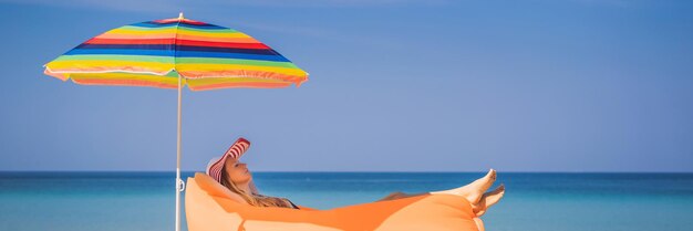 Retrato de estilo de vida de verano de una chica guapa sentada en el sofá inflable naranja en la playa de