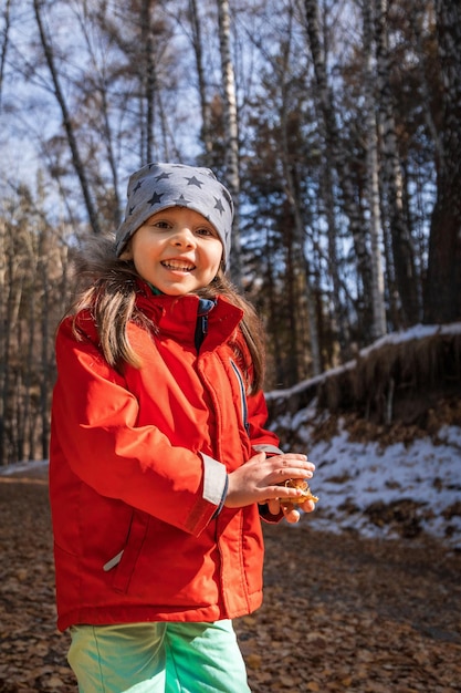 Retrato de estilo de vida vertical de una niña sonriente en edad preescolar en el bosque de finales de otoño