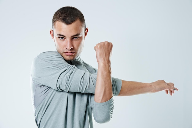 Retrato de estiramiento y hombre con entrenamiento de bienestar y atleta en fondo blanco de estudio Cara de persona y modelo con entrenamiento de ejercicio y desafío con rutina de cardio y equilibrio con fitness