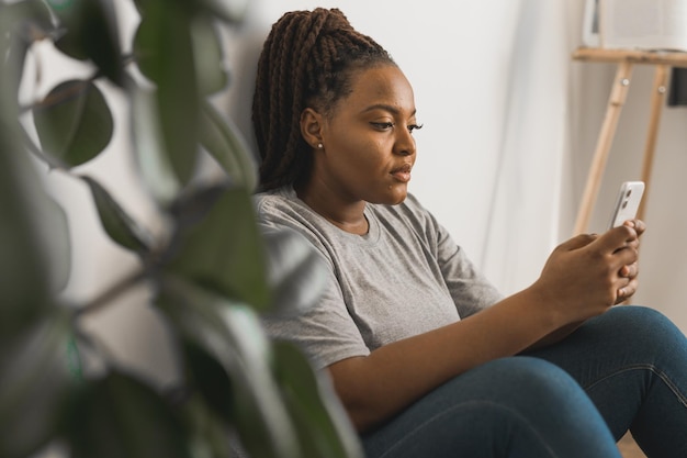 Retrato de una estudiante afroamericana vestida de manera informal sosteniendo un teléfono móvil y escribiendo