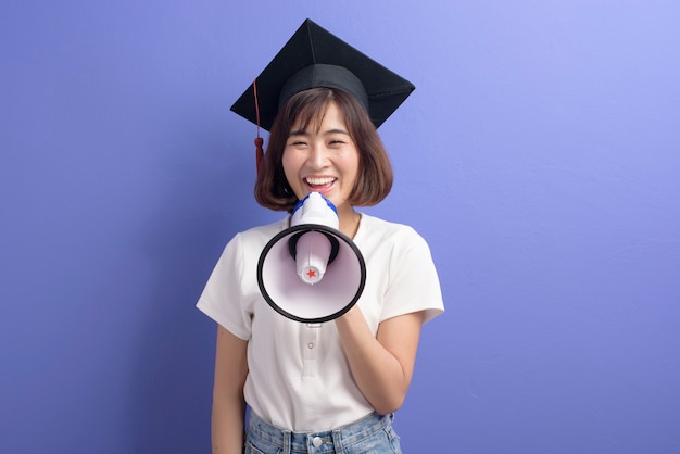 Un retrato de estudiante asiático graduado con megáfono aislado púrpura