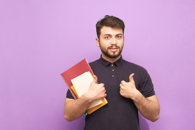 Retrato de un estudiante con barba de pie con libros y cuadernos en sus manos