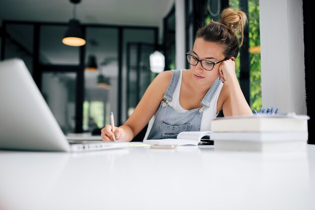 Retrato del estudiante cansado que se sienta en las notas de la escritura del café o del estudio y los libros de lectura.