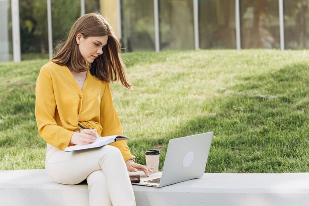 Retrato de una estudiante enfocada haciendo la tarea junto a una computadora portátil adolescente escribiendo en una nota