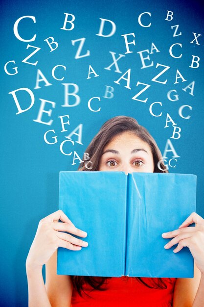 Foto retrato de un estudiante escondido detrás de un libro azul sobre fondo azul.