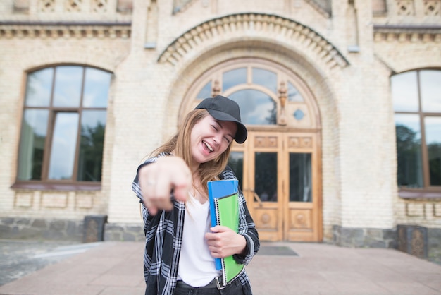 Retrato de un estudiante feliz con libros y cuadernos en las manos del fondo del edificio universitario.