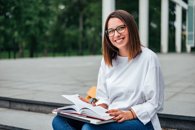 Retrato de un estudiante feliz que se sienta en las escaleras, sonriendo en la cámara.