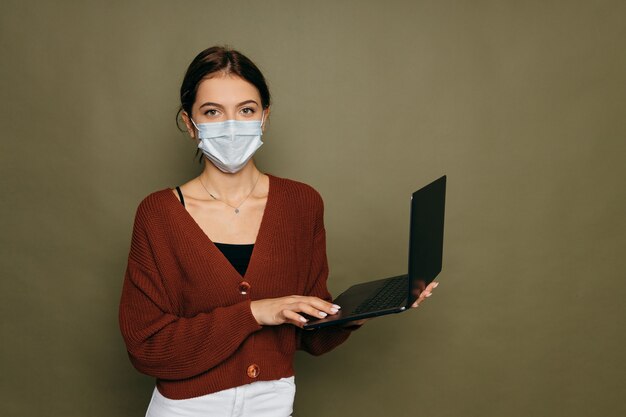 Retrato de una estudiante en una máscara protectora con una computadora portátil sobre un fondo verde. Foto de alta calidad