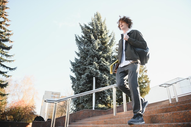 Retrato de un estudiante masculino feliz de pie en el campus con una bolsa