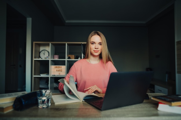 Foto retrato de una estudiante positiva sentada en casa en el trabajo con libros portátiles y portátiles