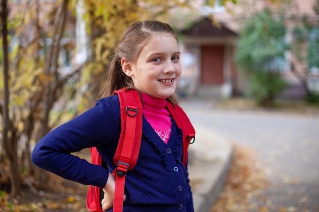 Retrato de estudiante de primaria con maletín rojo en otoño da