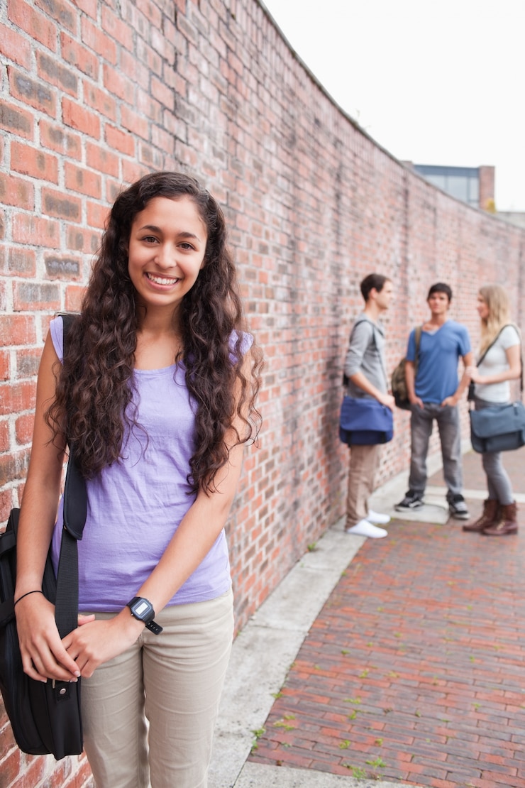 Foto retrato de una estudiante sonriente posando mientras sus amigos están hablando