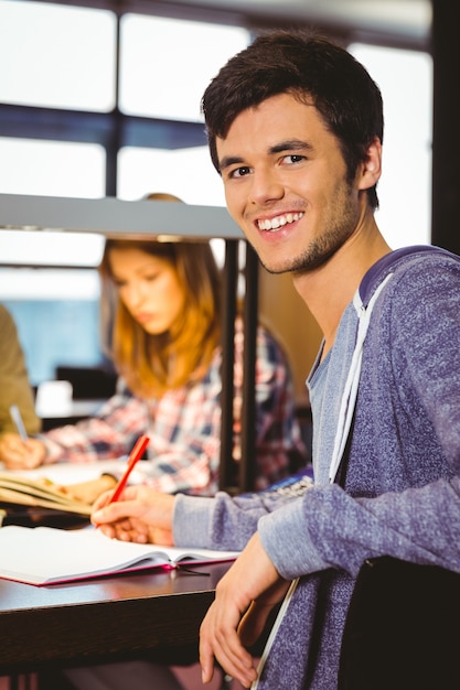 Foto retrato de un estudiante sonriente sentado en el escritorio mirando a cámara