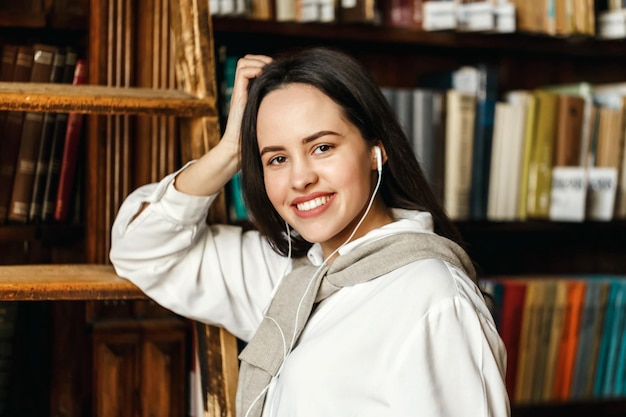 Retrato de estudiante universitario en auriculares de pie cerca de las estanterías