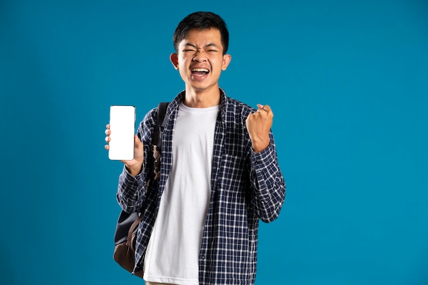 Retrato de estudiante varón satisfecho celebrando el éxito mientras sostiene el teléfono celular