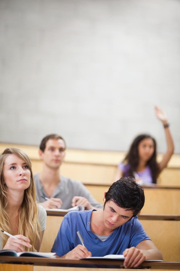 Foto retrato de estudiantes tomando notas mientras su compañera de clase levanta su mano