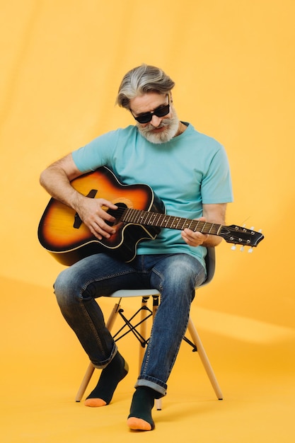 Retrato de estudio de un anciano canoso con gafas de sol tocando la guitarra