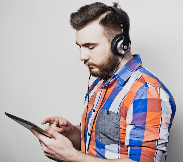 Retrato de estudio de un apuesto hombre barbudo que usa una tableta con auriculares sobre un fondo gris claro