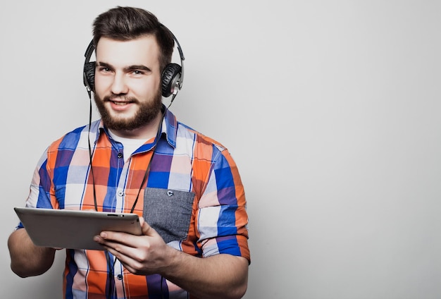 Foto retrato de estudio de un apuesto hombre barbudo que usa una tableta con auriculares sobre un fondo gris claro