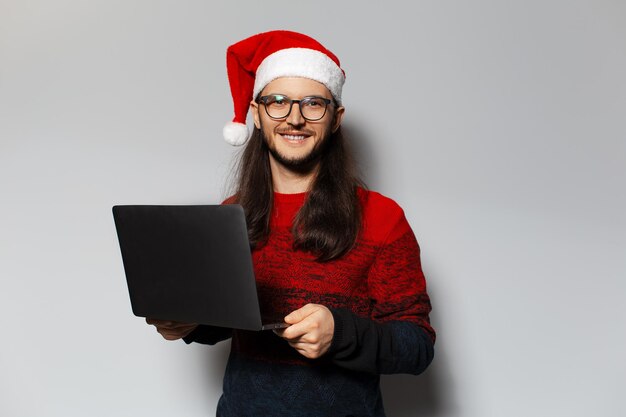 Retrato de estudio de un apuesto hombre sonriente sosteniendo un portátil en las manos con sombrero de Santa Claus Concepto de Navidad Fondo blanco