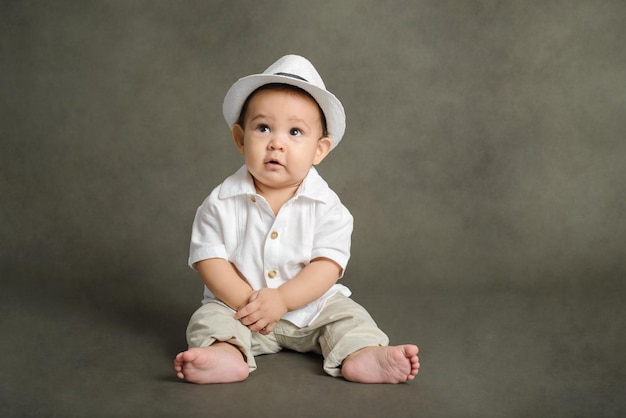 Retrato de estudio de un bebé sonriente con sombrero blanco sentado en el suelo