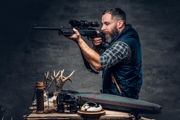 Retrato de estudio de un cazador moderno barbudo con su trofeo sostiene un rifle.