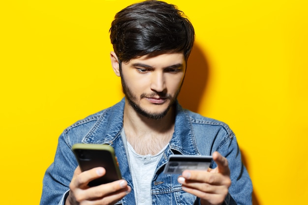 Retrato de estudio de chico joven con smartphone y tarjeta de crédito sobre fondo amarillo.