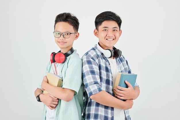 Retrato de estudio de colegiales felices con auriculares de pie con libros de estudiantes y sonriendo