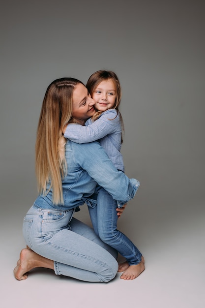 Retrato de estudio de feliz madre adulta en mezclilla abrazando a su pequeña hija también vistiendo jeans y camisa de mezclilla.