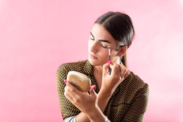 Retrato de estudio con fondo rosa de un adolescente varón poniéndose maquillaje