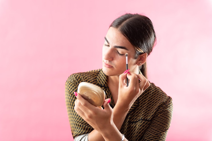 Foto retrato de estudio con fondo rosa de un adolescente varón poniéndose maquillaje